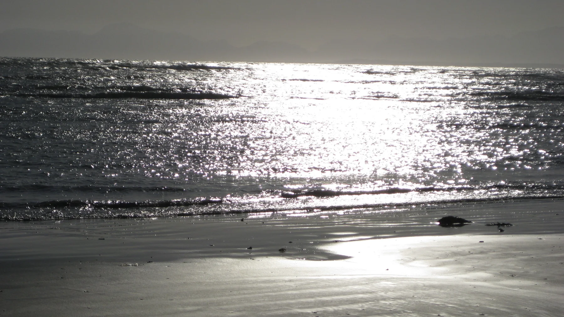Strong sunlight creates a silver reflection across waves and wet sand.