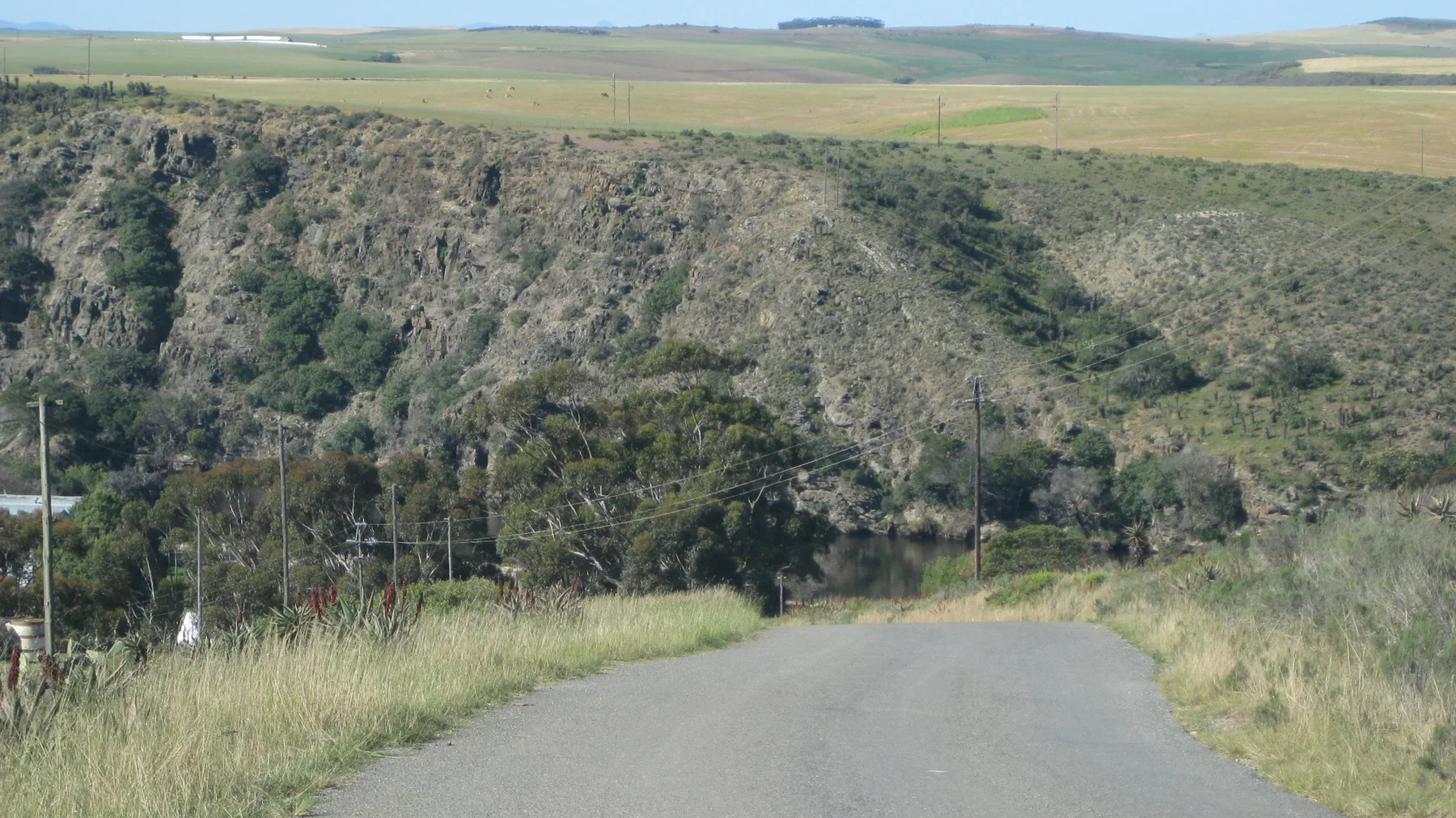 A narrow road descends beside grass toward a steep valley wall.