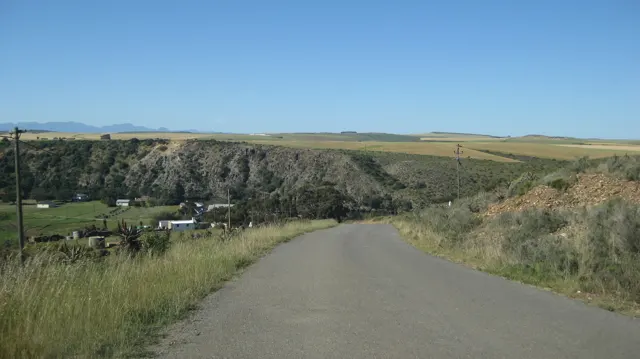 A paved lane slopes toward a green valley beneath open fields.