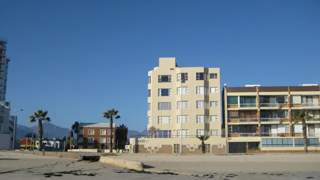 Pale apartment facades stand along a sandy waterfront.