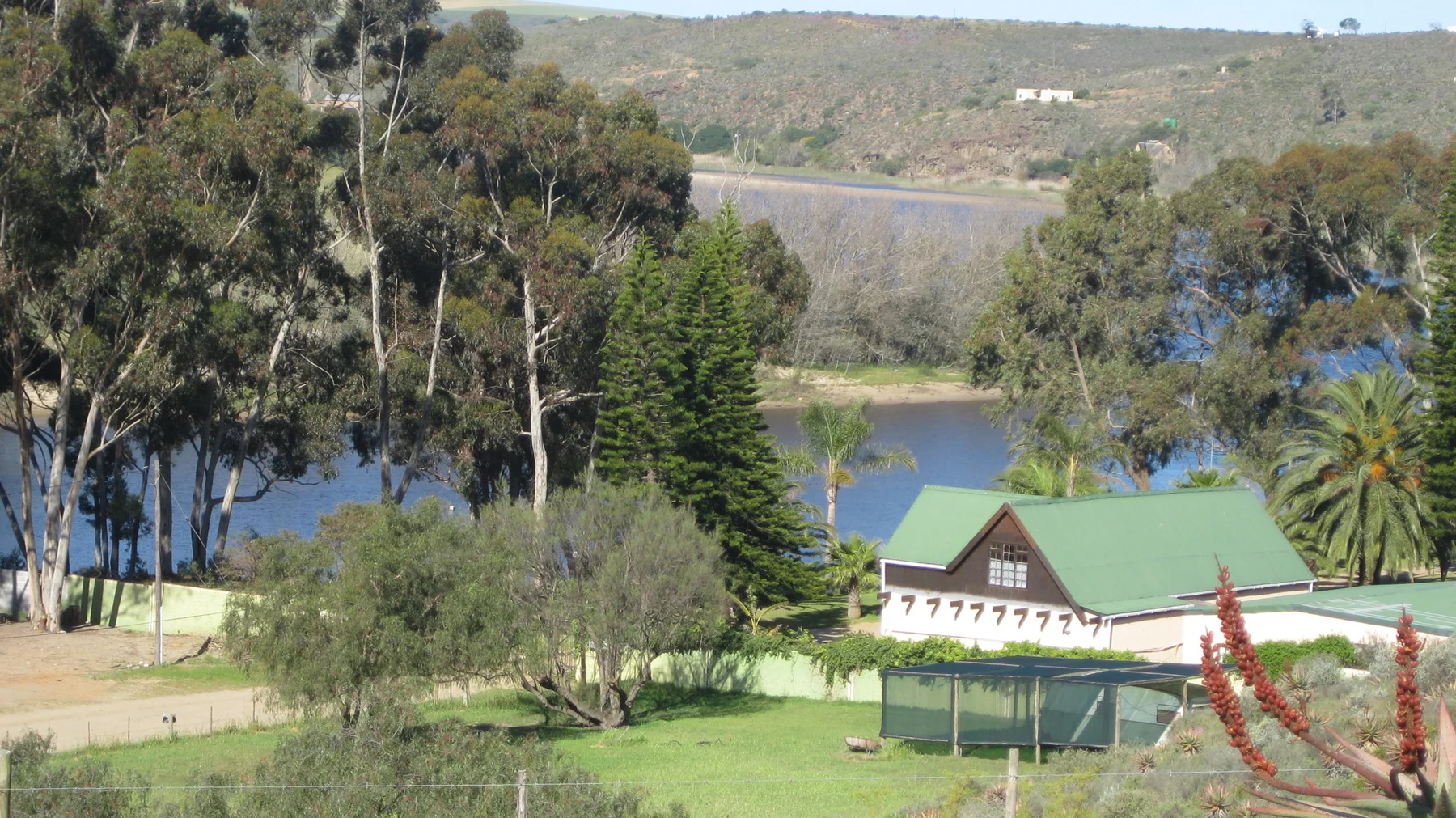Green-roofed buildings sit among trees above a calm watercourse.