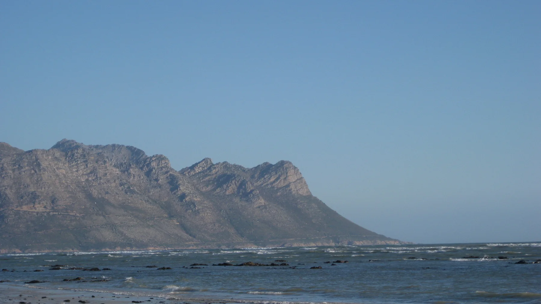 A rugged mountain range rises beyond dark shallow sea water.
