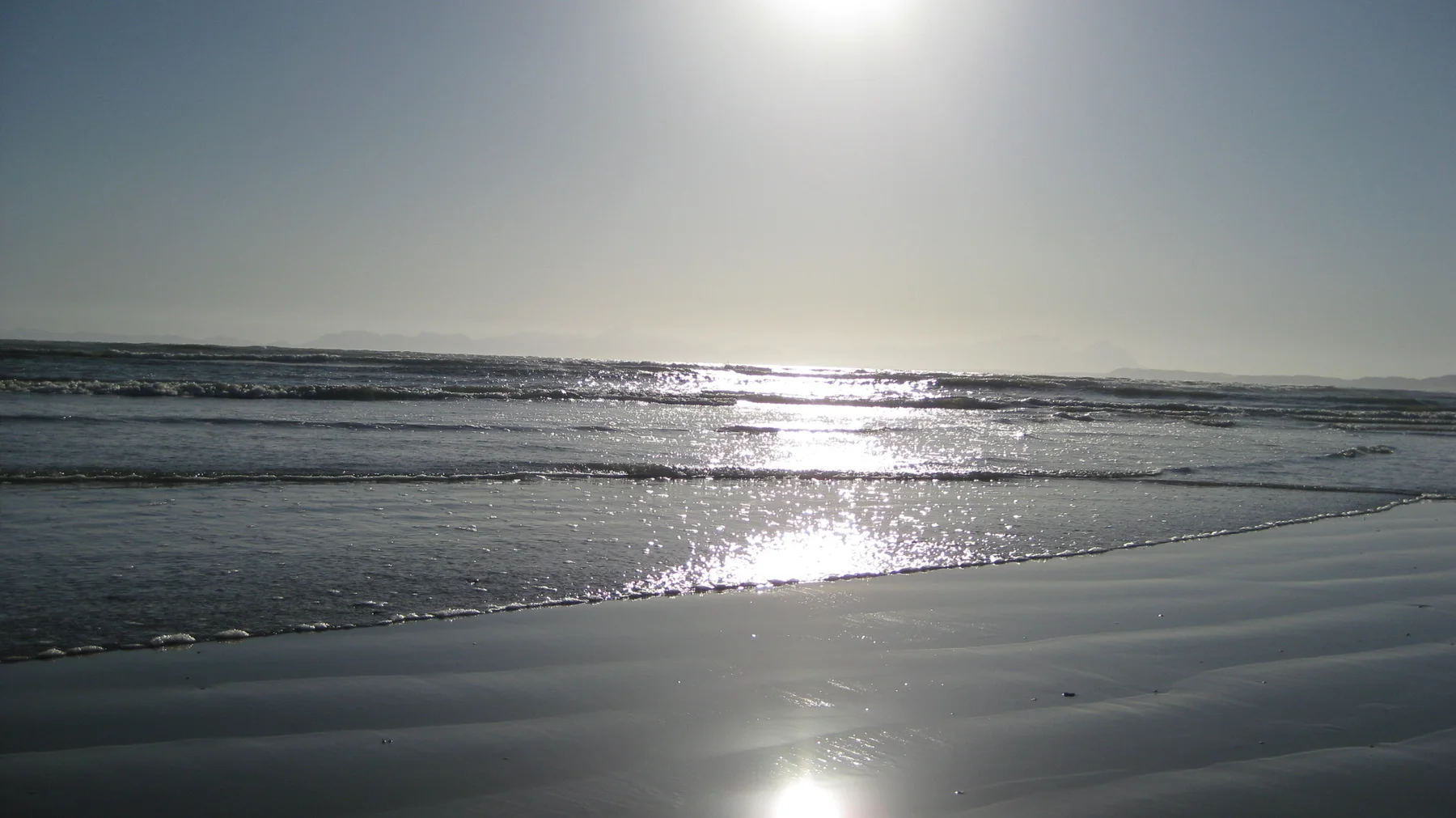 Sunlight makes a silver path across shallow surf and wet beach.