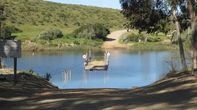 A small ferry platform sits on calm water between dirt-road landings.