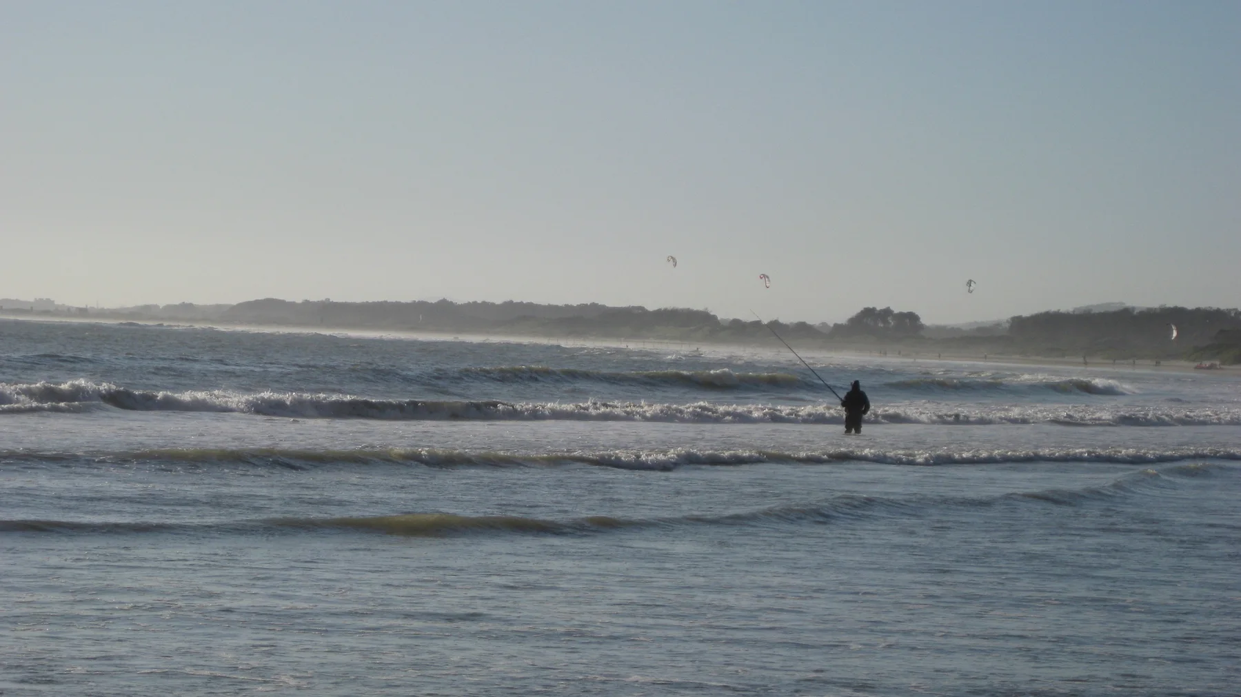 A distant figure stands beyond low breaking waves.