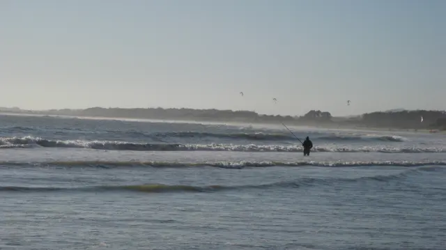 A distant figure stands beyond low breaking waves.