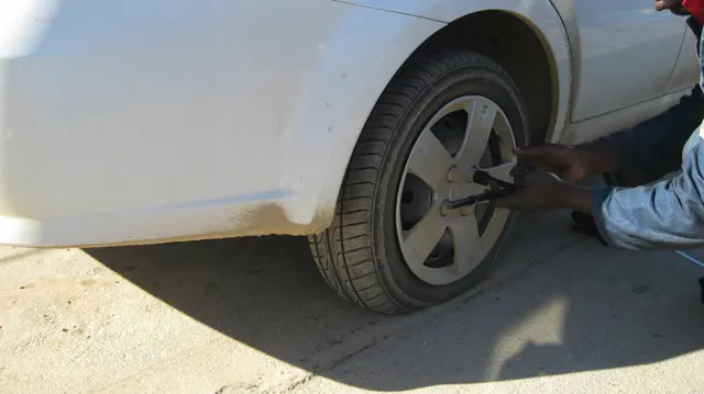 A person works beside the rear wheel of a white car.