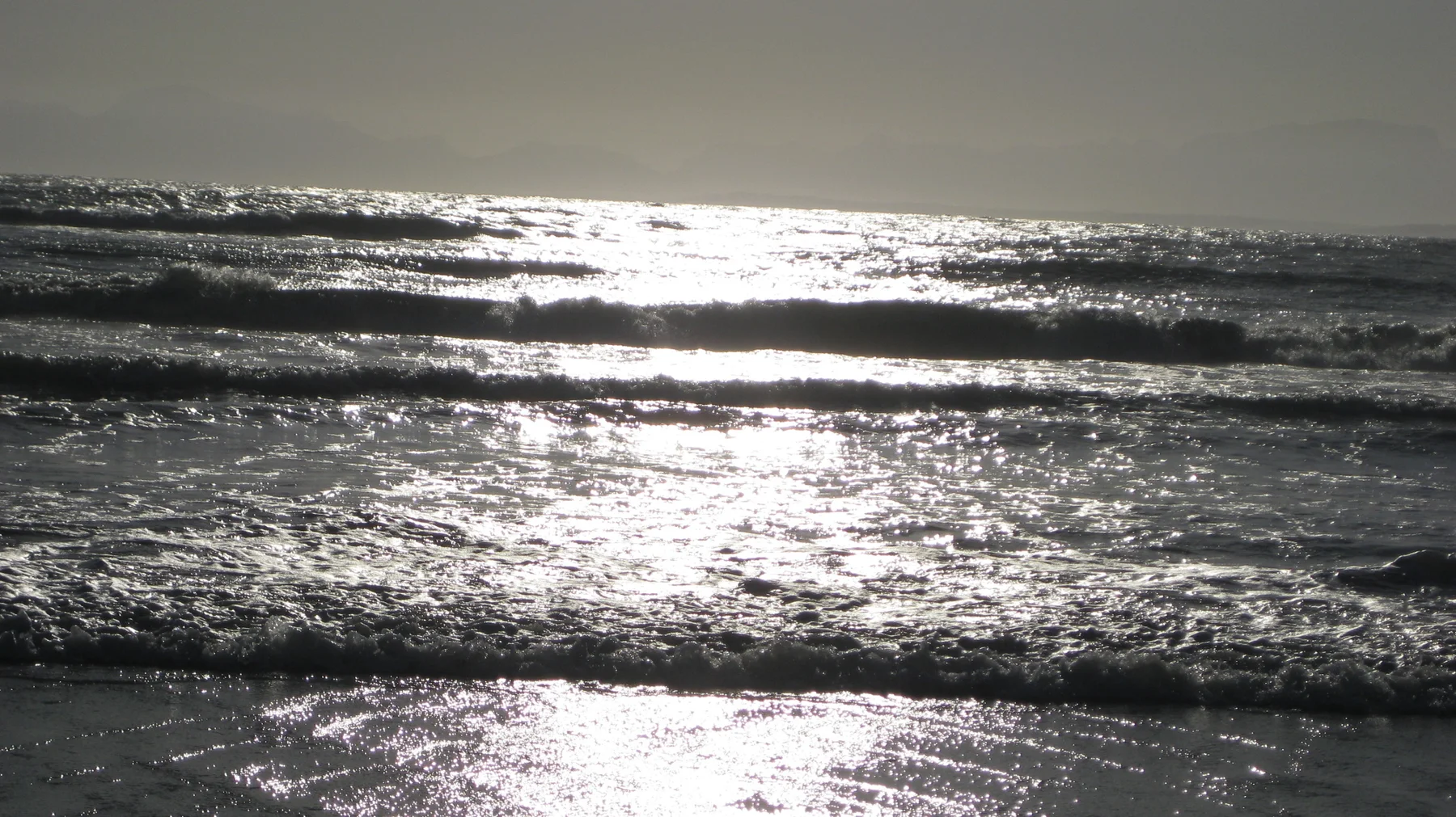 Sunlight forms bright bands across small breaking waves.