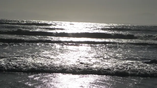 Sunlight forms bright bands across small breaking waves.