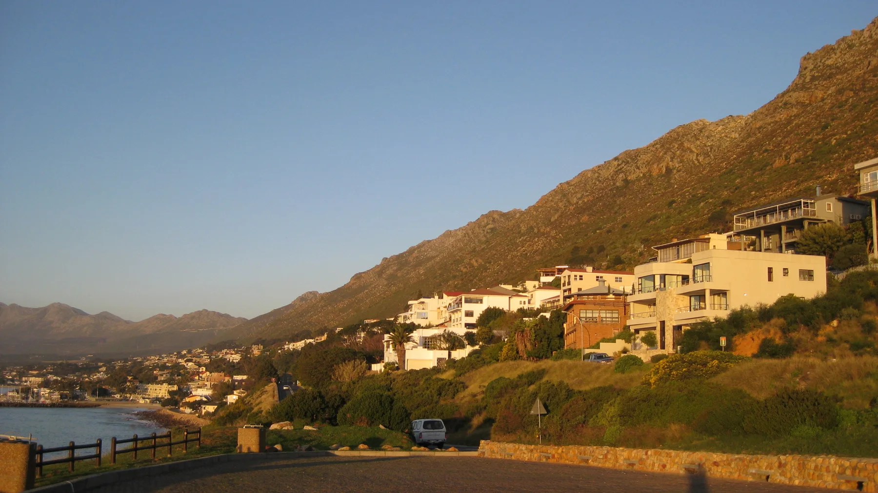 Evening light warms houses built along a steep coastal hillside.