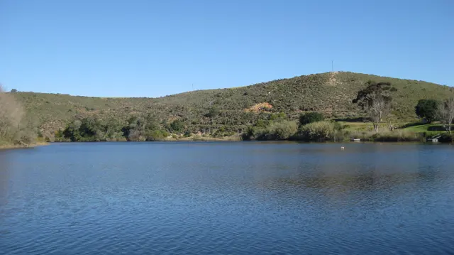 Calm blue river water lies below low grassy hills.