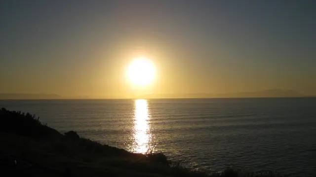 A low golden sun casts a straight reflection across the sea.