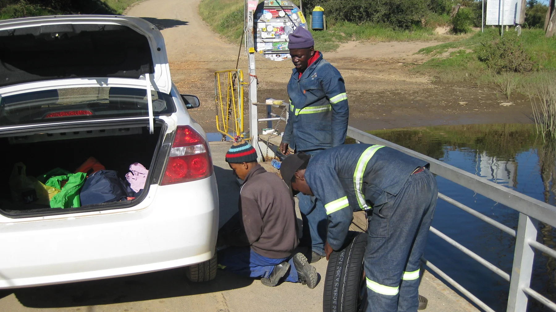 People stand beside an open car trunk on a small ferry deck.