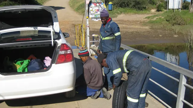 People stand beside an open car trunk on a small ferry deck.