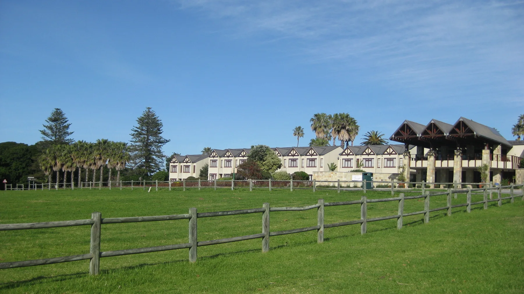 Houses and palms stand beyond a broad fenced green field.