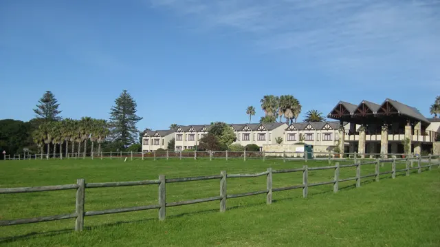 Houses and palms stand beyond a broad fenced green field.