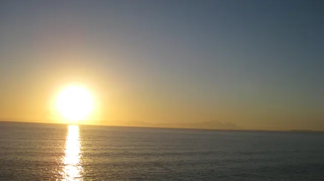 A low sun glows above the horizon with a long water reflection.