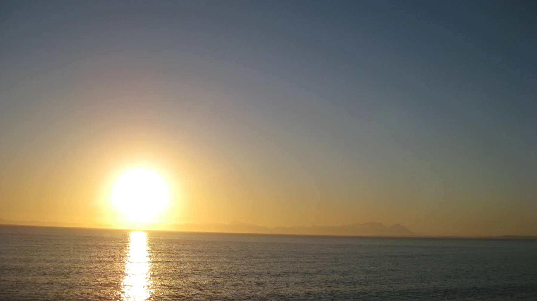 A bright golden sun sits above a flat ocean horizon.