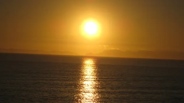 An orange sun glows above a shimmering vertical reflection.