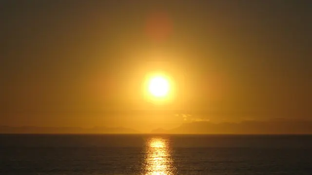 A bright orange sun hangs above the darkening sea.