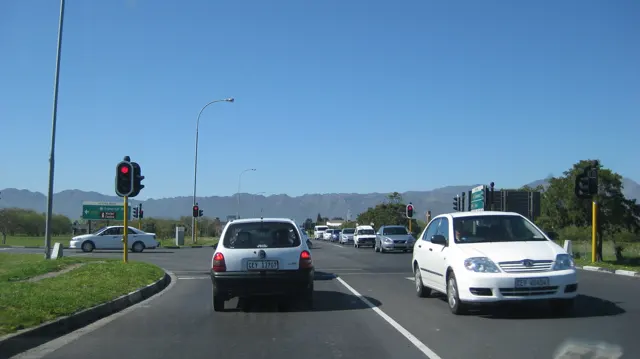 Cars gather at traffic lights beneath a clear sky and distant mountains.
