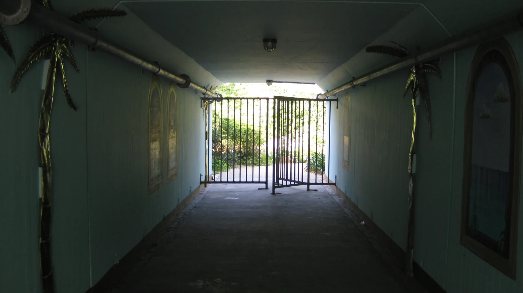 A dim covered passage leads toward a bright metal gate.