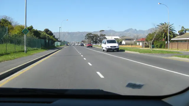 A broad road leads toward a long mountain range under blue sky.