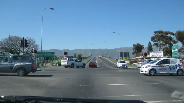 Cars cross a broad intersection beneath signs and streetlights.