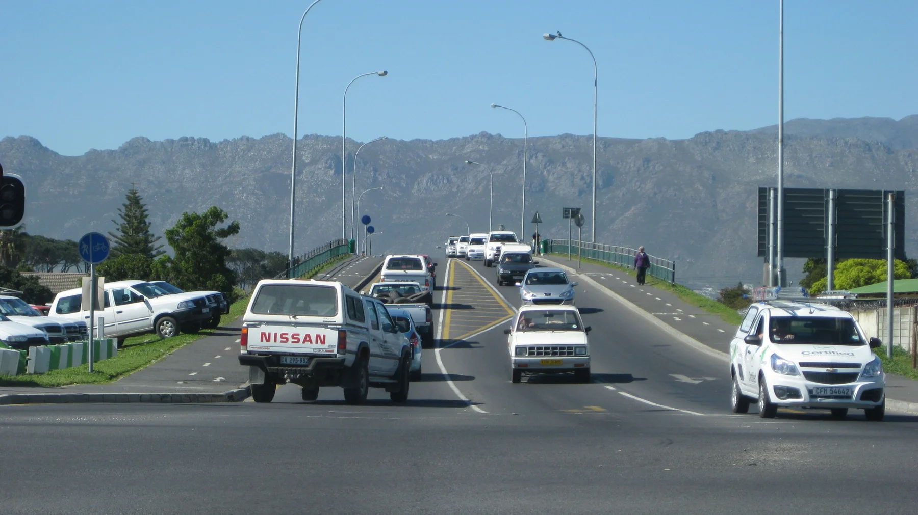 Vehicles climb an overpass with a rugged mountain range behind.