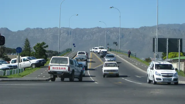 Vehicles climb an overpass with a rugged mountain range behind.