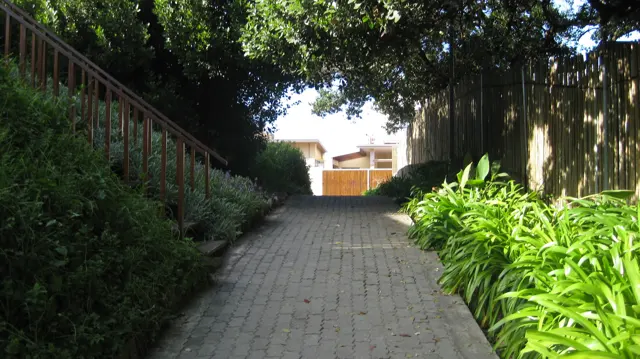 A brick walkway rises between leafy borders and railings.