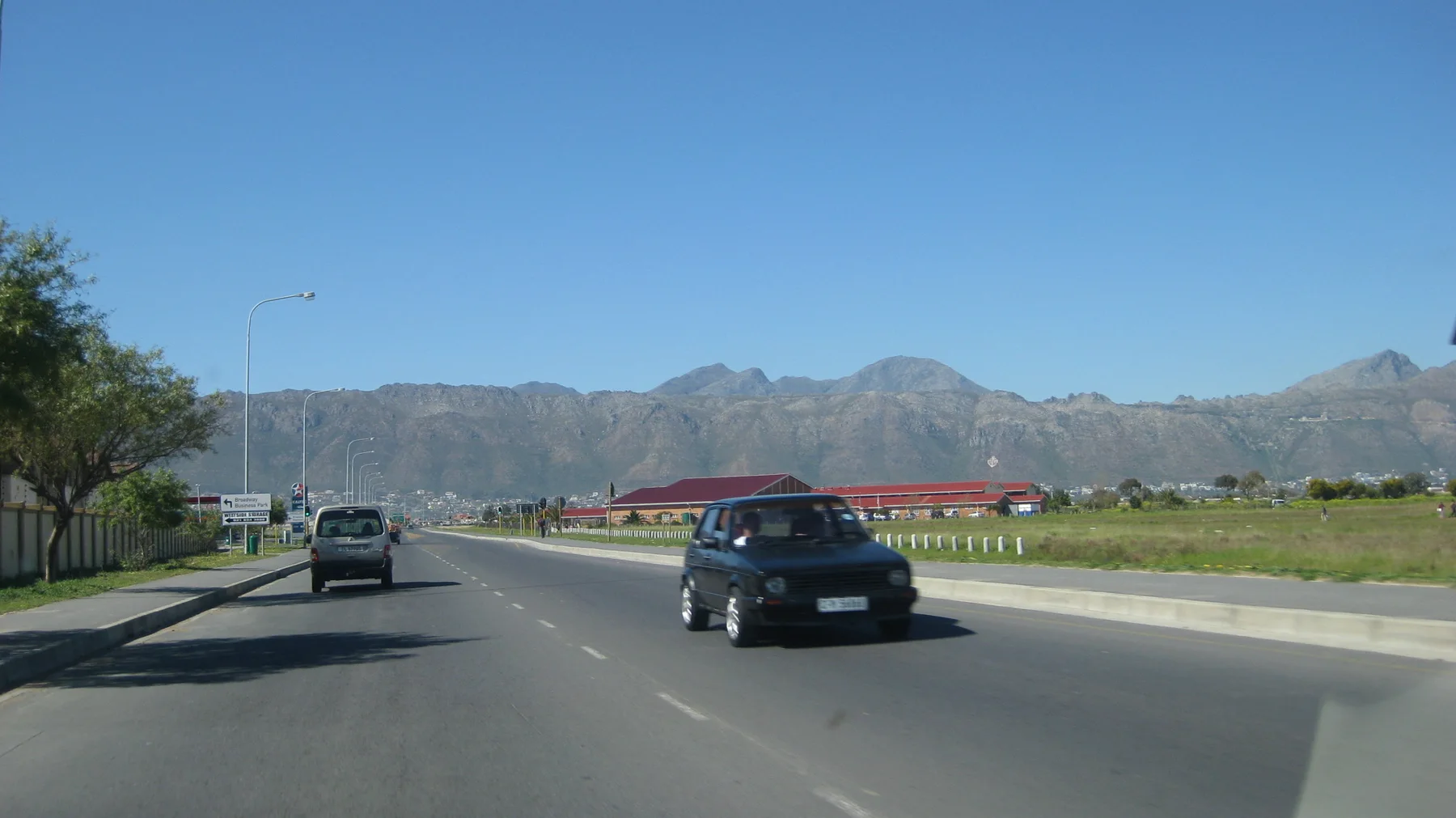 Traffic moves along a sunny road toward a continuous mountain ridge.