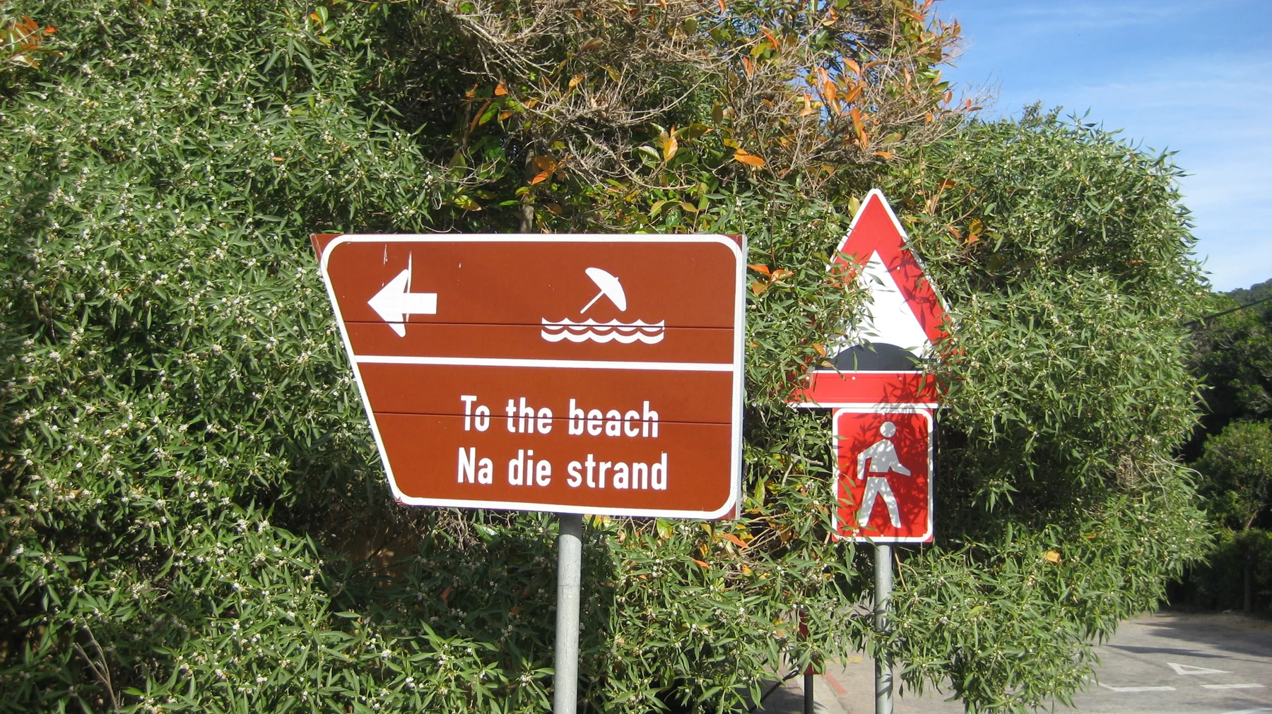 A brown bilingual sign points left toward the beach.
