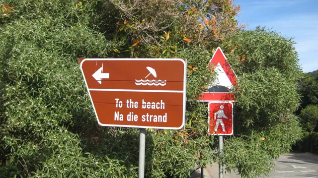 A brown bilingual sign points left toward the beach.