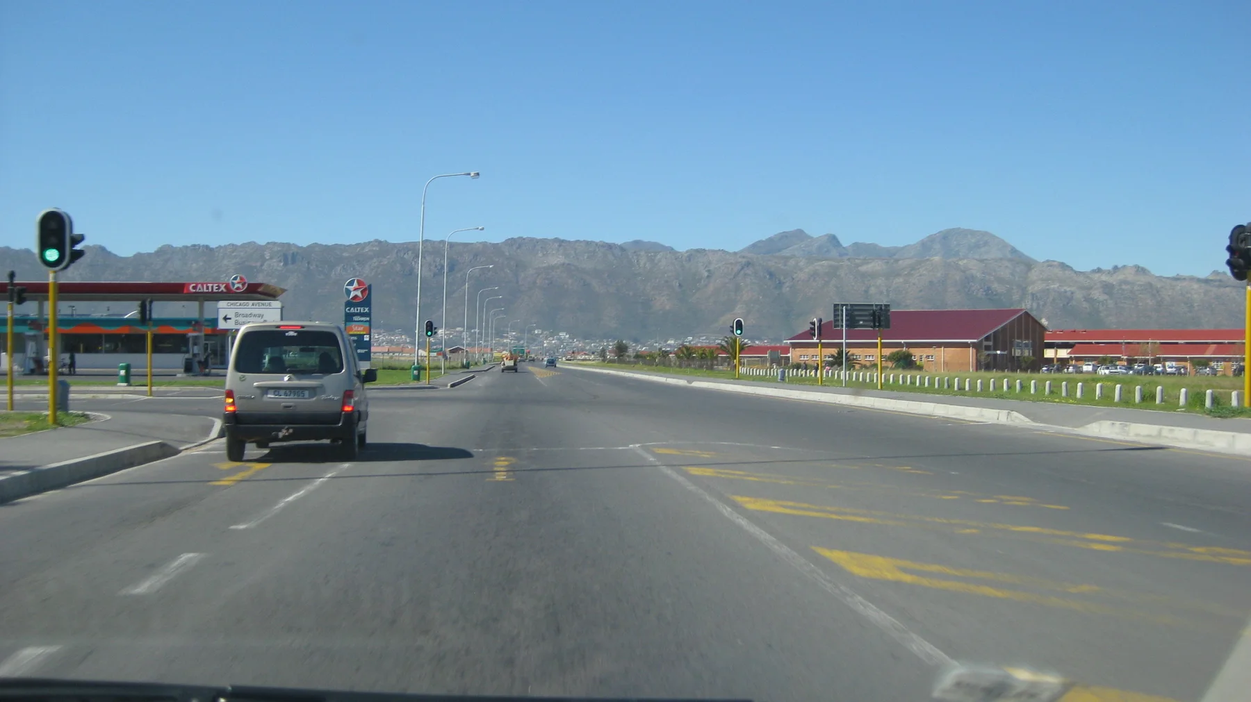 Traffic lights show green on a broad road below mountain ridges.
