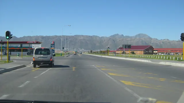 Traffic lights show green on a broad road below mountain ridges.