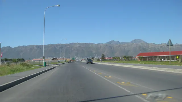 A wide road passes red-roofed buildings beneath a distant ridge.