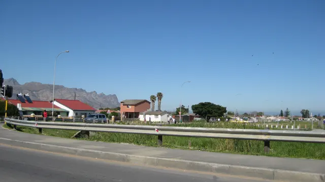 A guardrail borders a view of red roofs, palms and mountains.