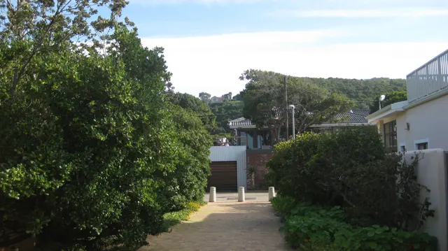 A paved passage runs between hedges and pale buildings.