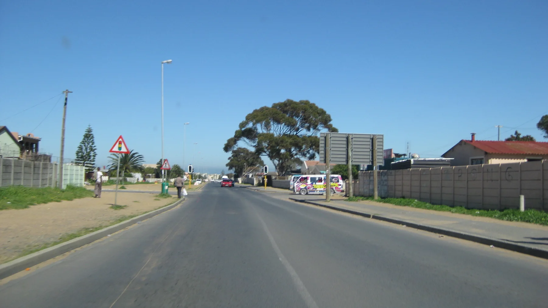 A road passes fences, signs and low buildings under clear sky.