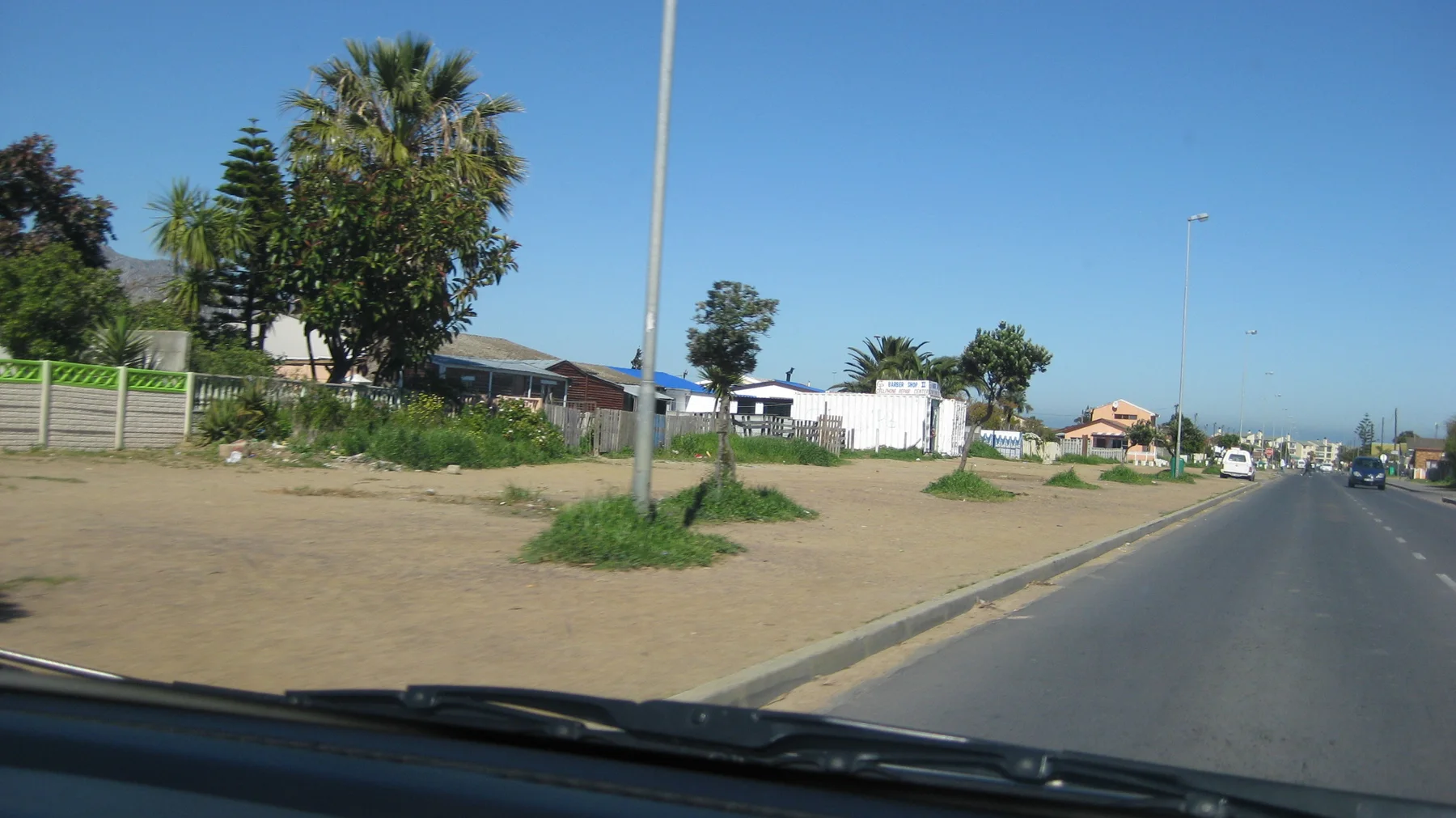 Palms rise beside houses and a broad sandy roadside verge.