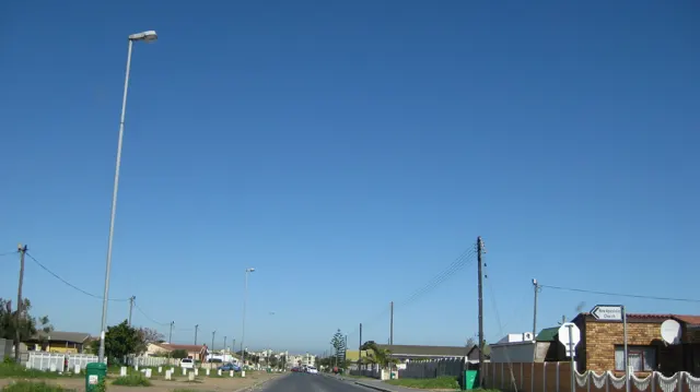 Tall streetlights rise above low roadside buildings and utility lines.