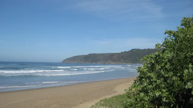 Waves wash a broad beach below a green headland.