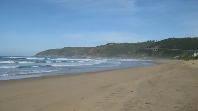 Footprints follow a broad sandy beach beside white waves.