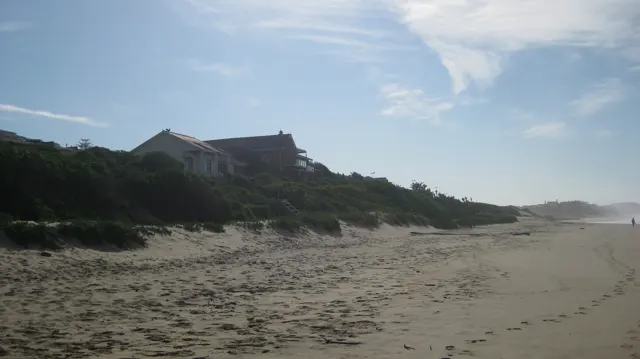 Coastal houses stand above a long sandy beach and low dunes.