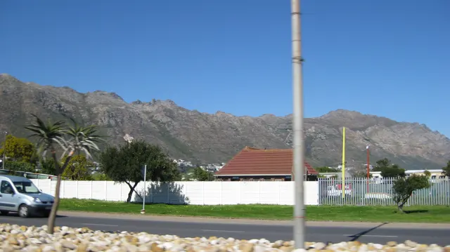 A red-roofed building stands behind a white wall below mountains.