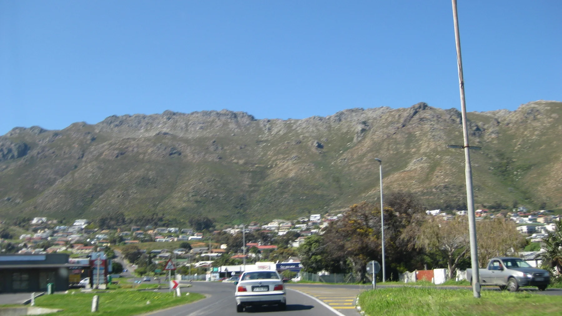 Cars follow a town road beneath a rugged mountain wall.