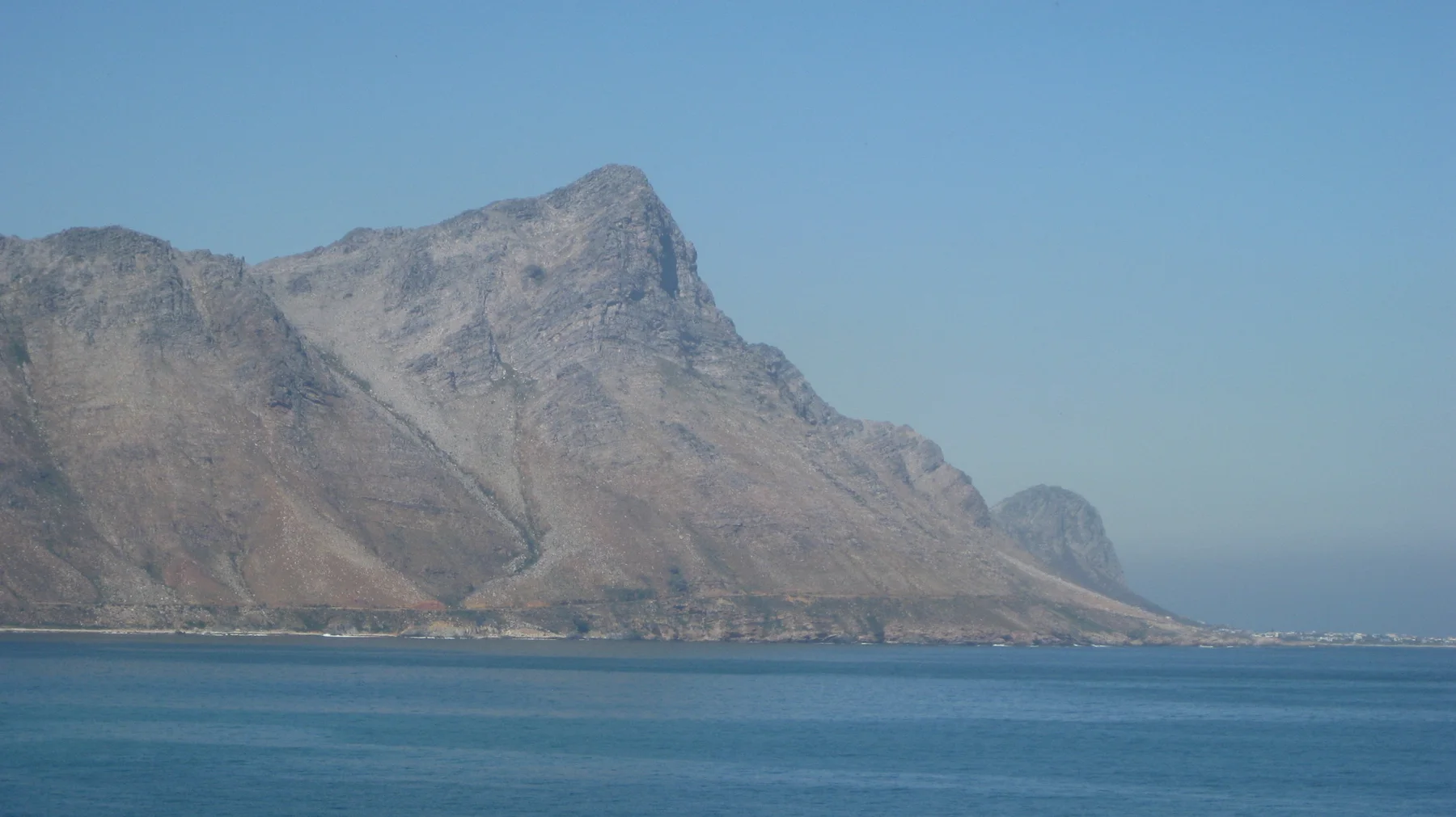 A steep rocky peak rises above calm blue water.