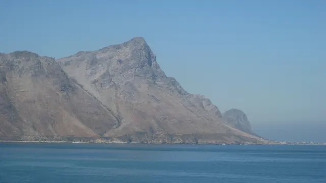 A steep rocky peak rises above calm blue water.