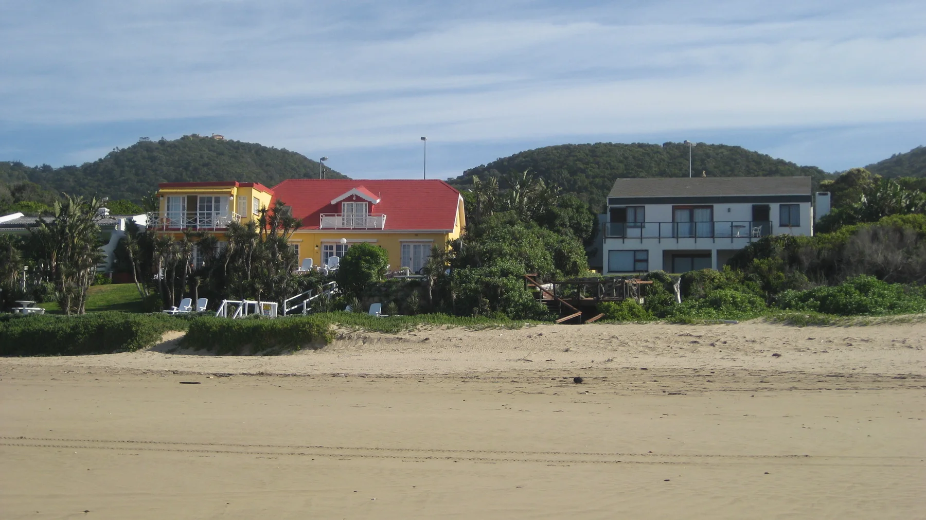 A red-roofed building and pale houses stand behind a sandy beach.